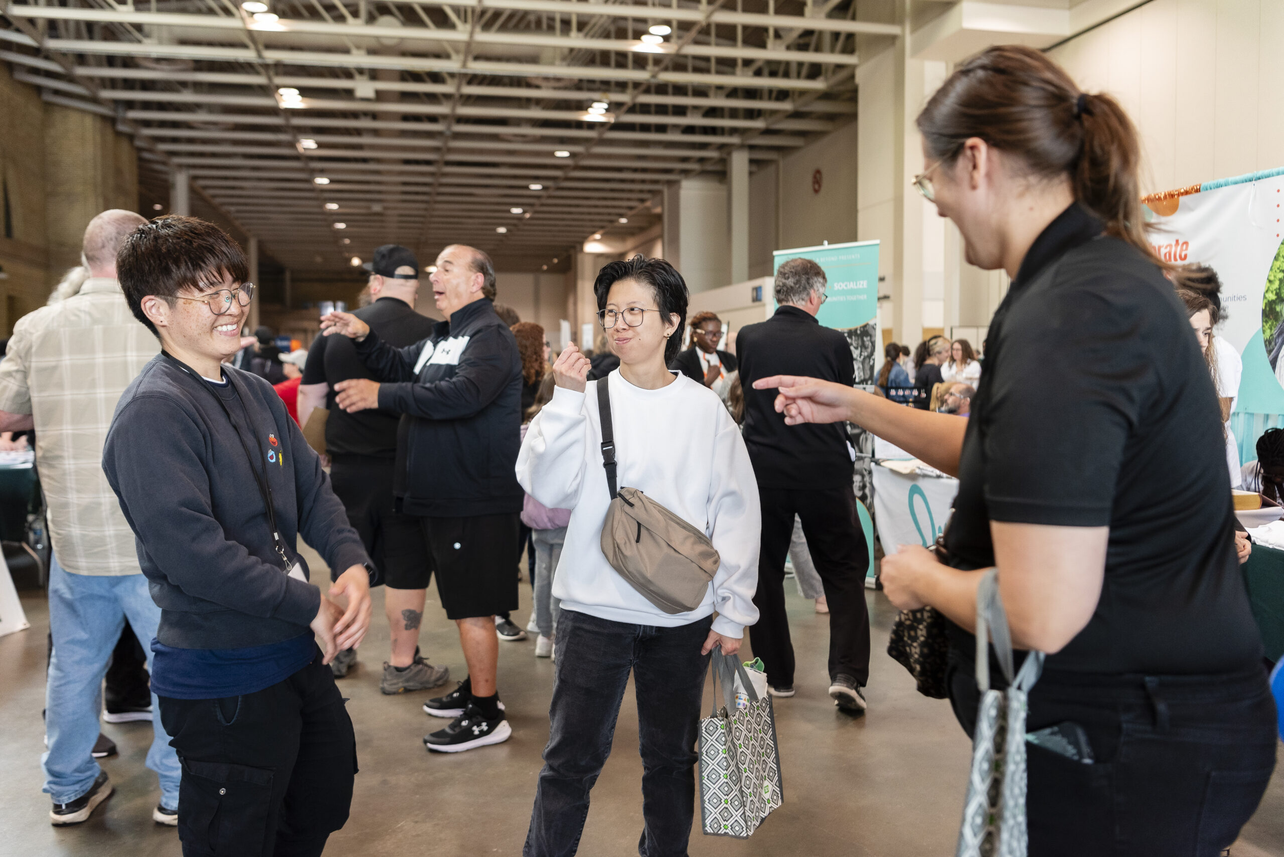 Three people having a conversation in sign language. There are people and various booths visible in the background.