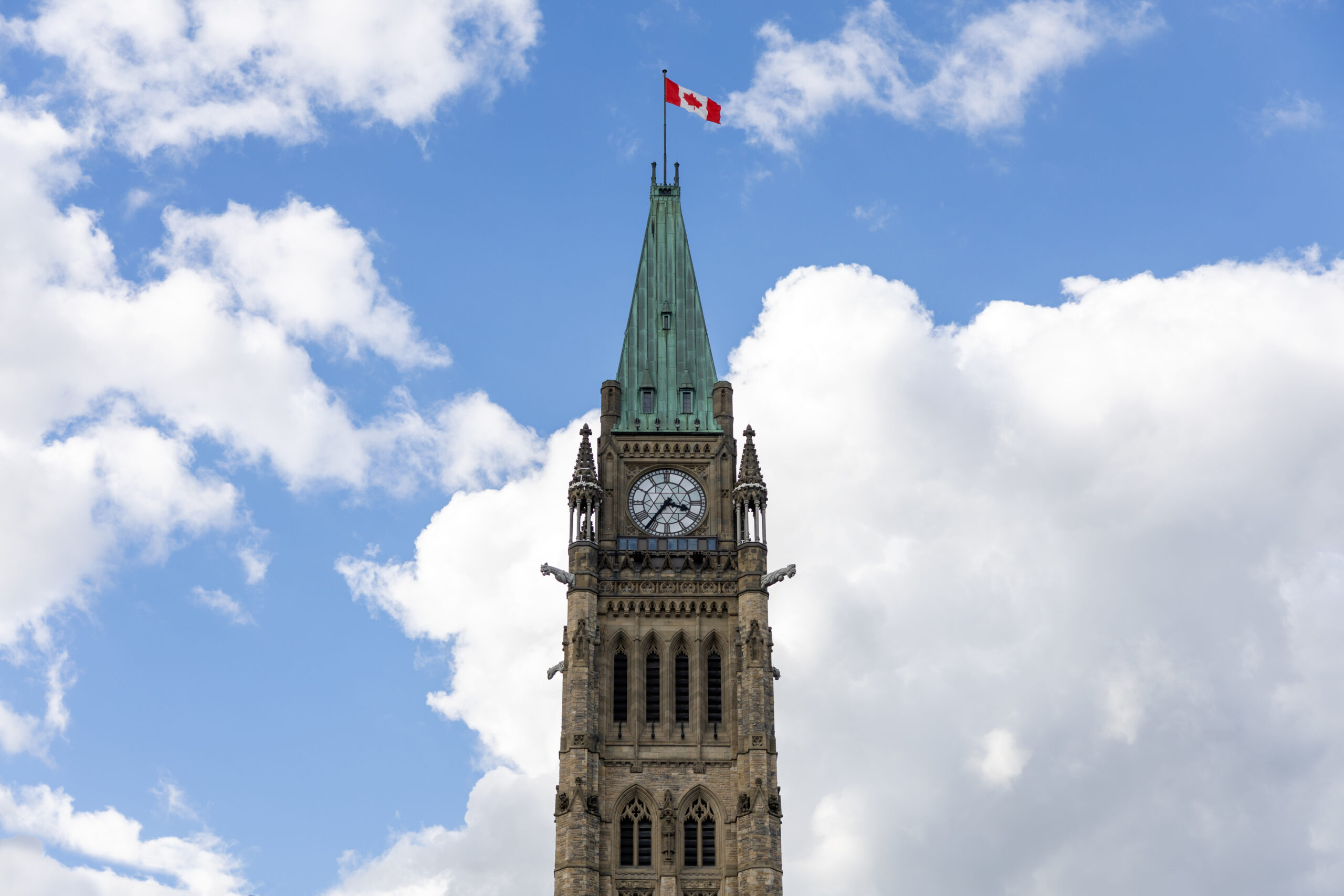 Parliament building with Canadian flag in Ottawa, Canada. Peace tower against blue sky with clouds.